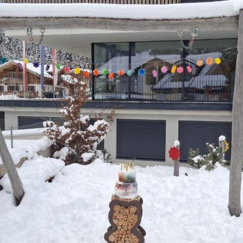 Bunte Eiskristalle hängen an einer Schnur entlang; an den Seiten sind zwei Luftballone angebunden; auf einem Holzbären steht ein Schneekuchen mit Tortenfontänen